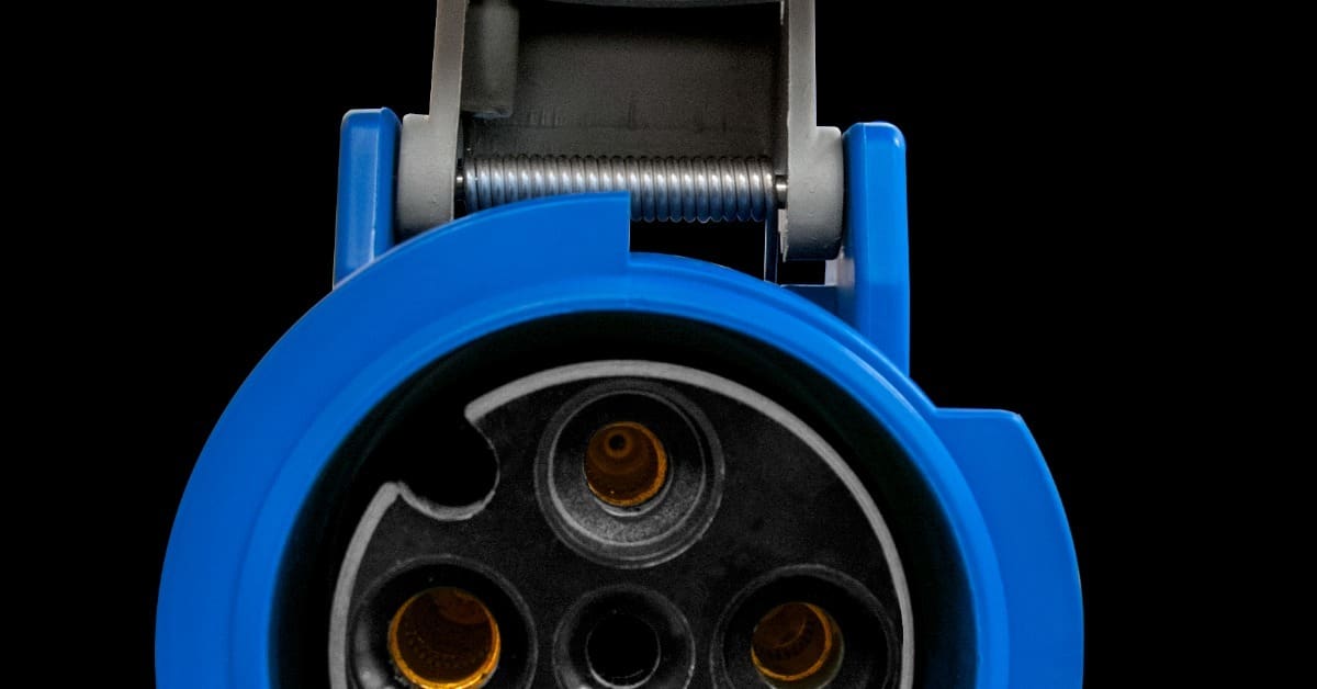 A blue industrial connector with an open gray cap exposing circular ports and metal contacts on a black background.