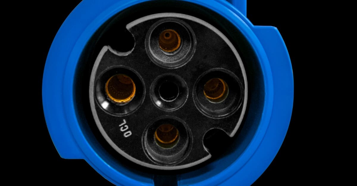 A blue circular plug end with a black face, four round contact openings, and small white letters on one side.