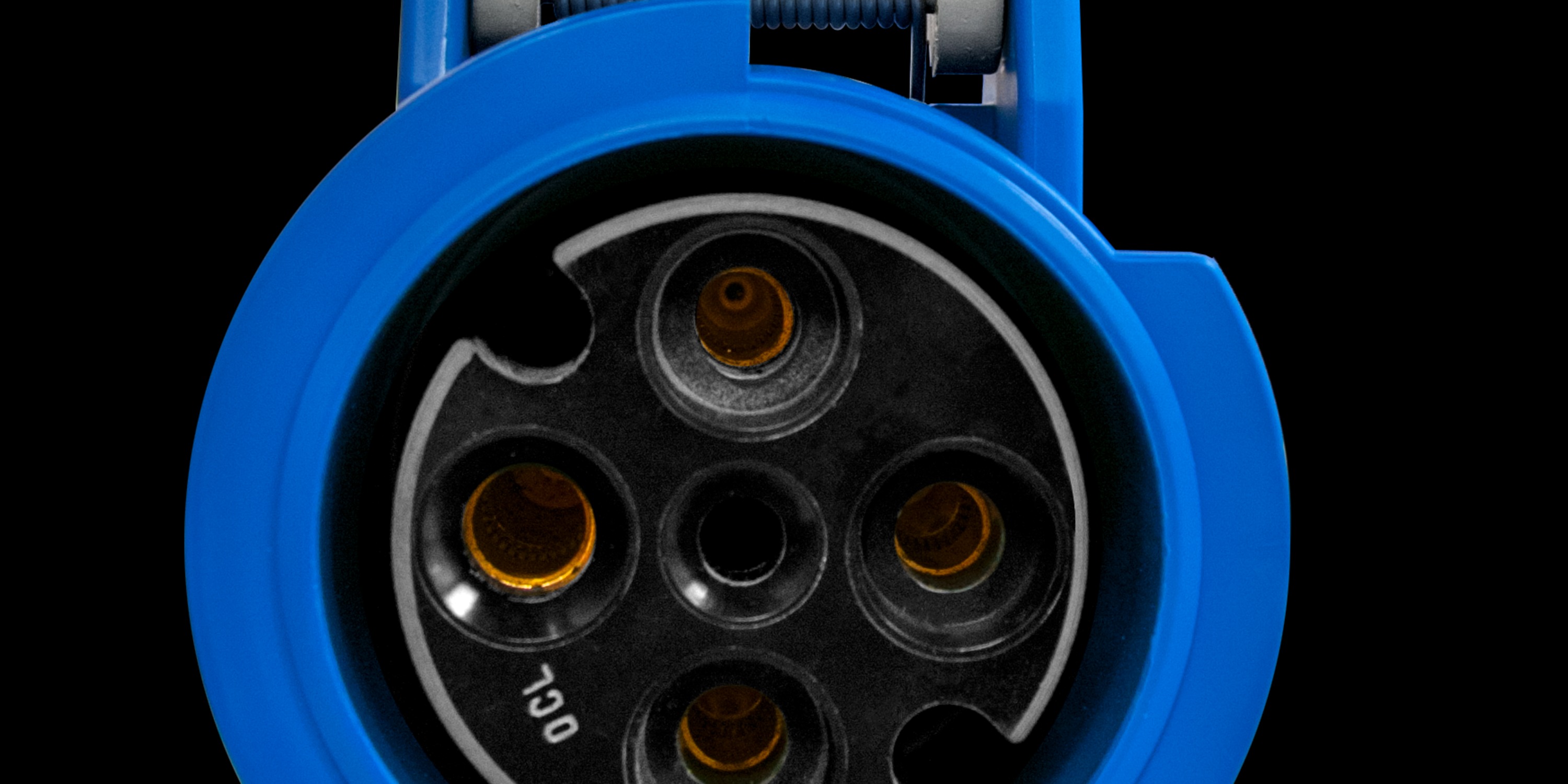 A blue IEC power cord connector with four brass contact openings inside a round black socket against a dark background.